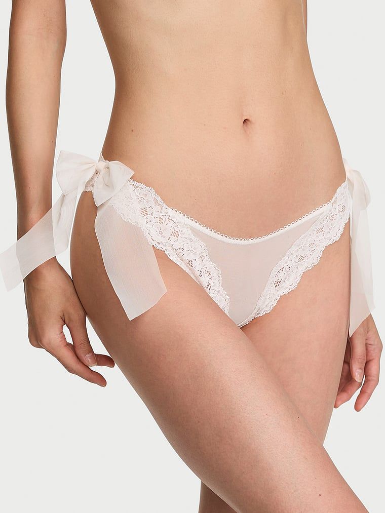 Brazilské kalhotky s mašlemi po stranách, krajka a síťovaná boční mašle. Produkt je bílý a pochází z kolekce Dream Angels.